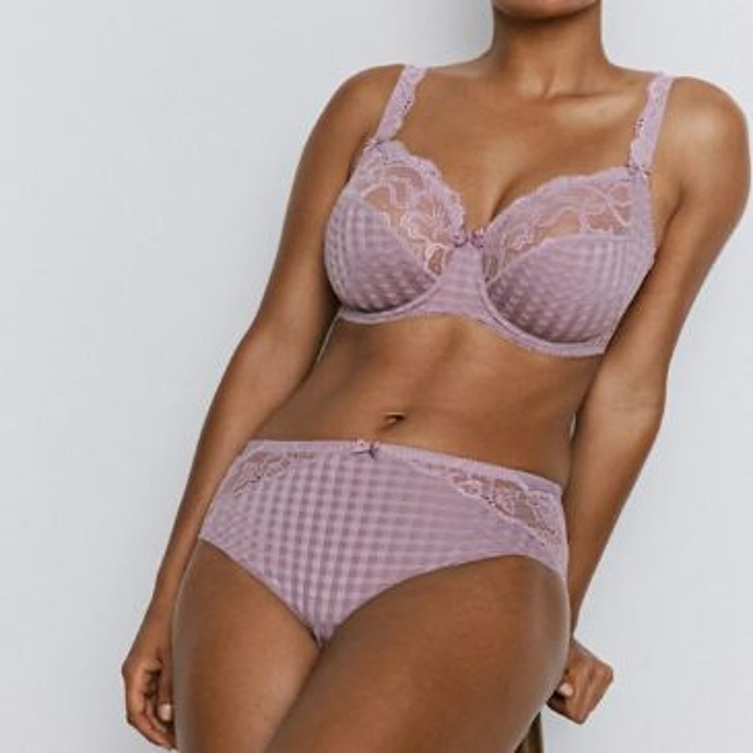 Un mannequin porte un soutien-gorge et une culotte mauves à petits carreaux ornés de dentelle, devant un fond uni clair.