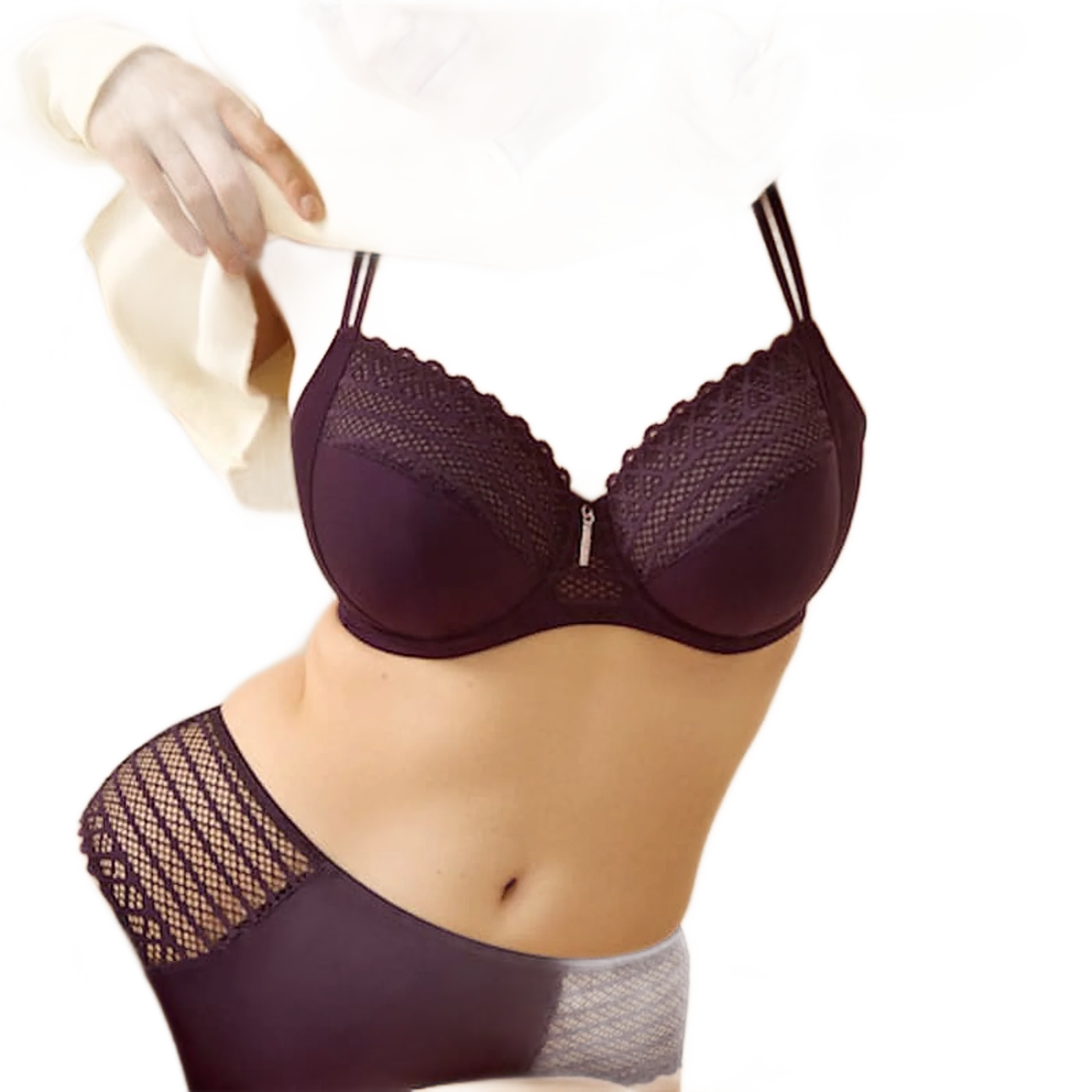 Une femme portant un soutien-gorge et une culotte prune ornés de dentelle géométrique remonte un gilet jaune pâle devant un mur beige.