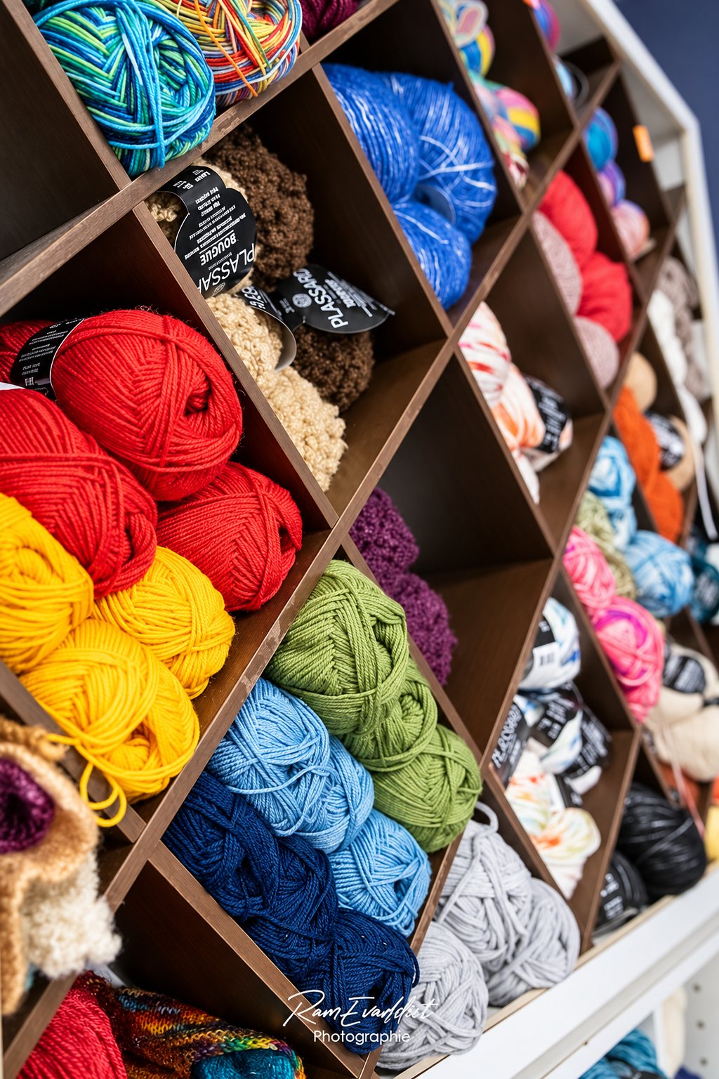 Une étagère en bois à alvéoles en losange présente des pelotes de laine de couleurs variées : rouge, jaune, vert, bleu et gris.