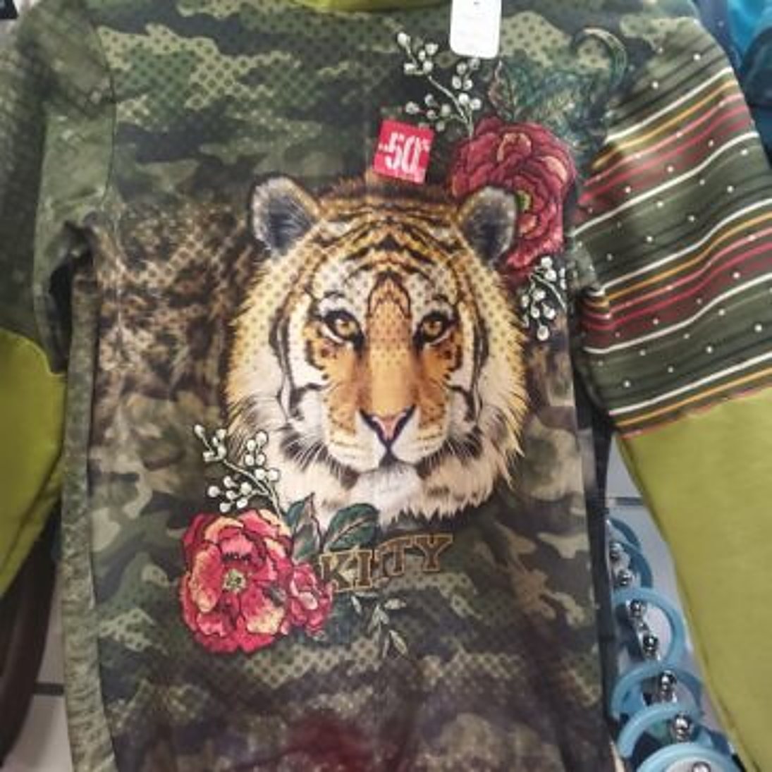 Un haut à motif camouflage vert avec un portrait de tigre entouré de roses rouges, manches rayées et étiquette de réduction -50 %.